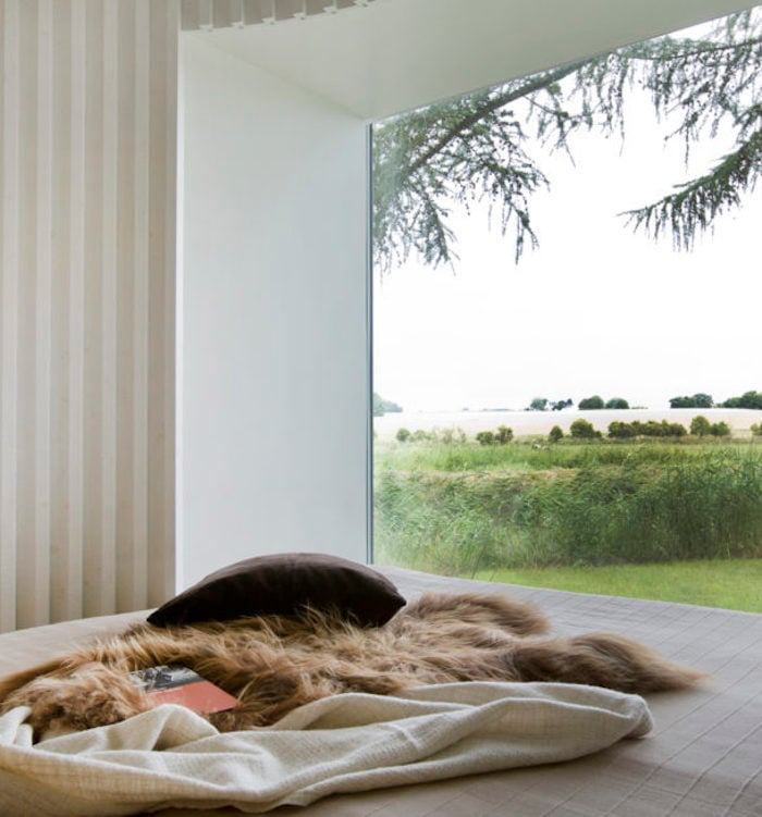 maison ronde chambre fenetre lit vue sur foret matela fourrure coussins blanc bois