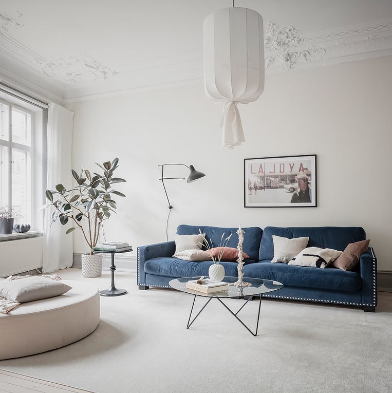 salon spacieux tapis extra large canapé bleu marine velours table basse verre pied métallique noire pièce lumineuse blanche