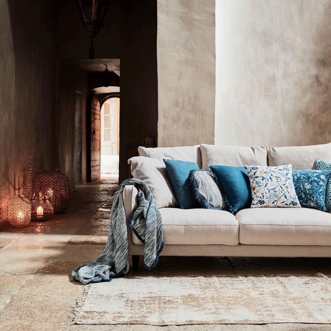 canapé lin beige mur brique pierre blanche coussin bleu