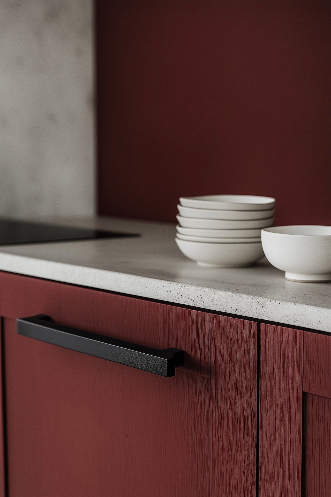 façade de cuisine rouge mat texturée avec poignée noire rectangulaire, plan de travail en pierre claire mouchetée, pile d'assiettes et bol en céramique blanche, mur rouge en arrière-plan flou