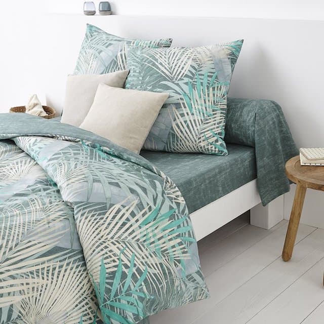 Chambre avec parure de lit tropicale et feuillage vert sur fond clair