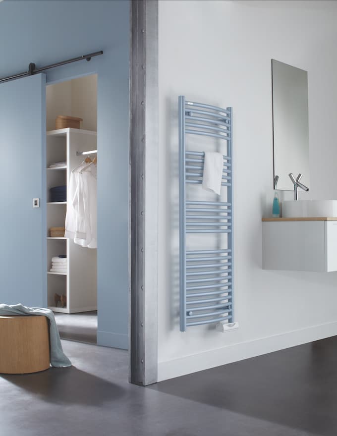 Radiateur sèche-serviettes bleu dans une salle de bain lumineuse avec meuble vasque blanc