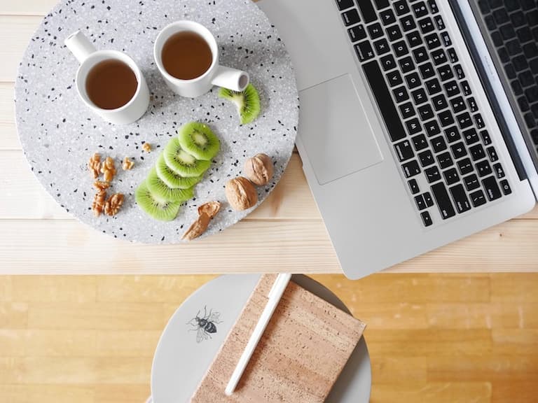 Pause thé à deux avec ordinateur, kiwi et vaisselle Serax sur une table blanche