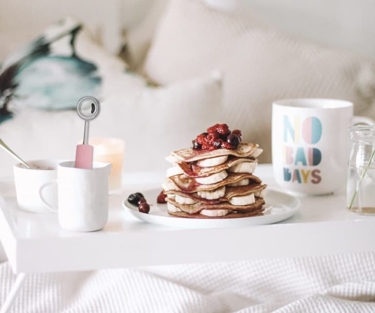 Pile de pancakes aux fruits rouges entourée de tasses blanches sur une table de petit-déjeuner