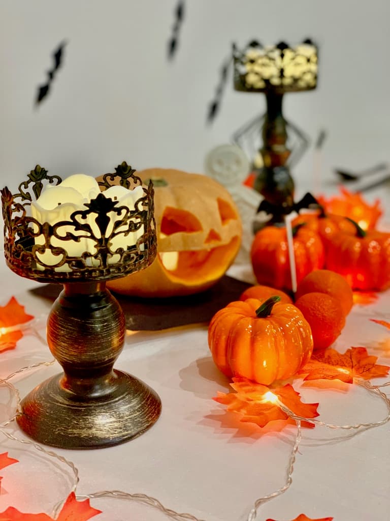 bougie à pile dans un chandelier noir entouré de mini citrouilles et d'une guirlande lumineuse
