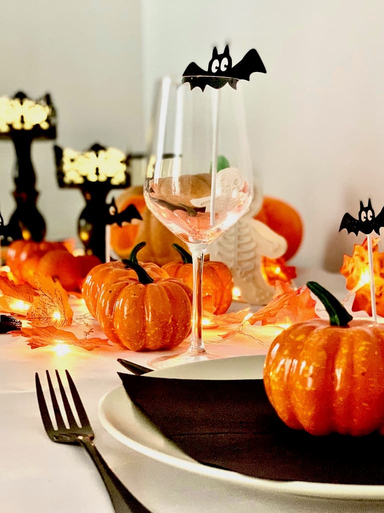 assiettes noires et orange, couverts noirs et petites citrouilles sur une table d'Halloween blanche