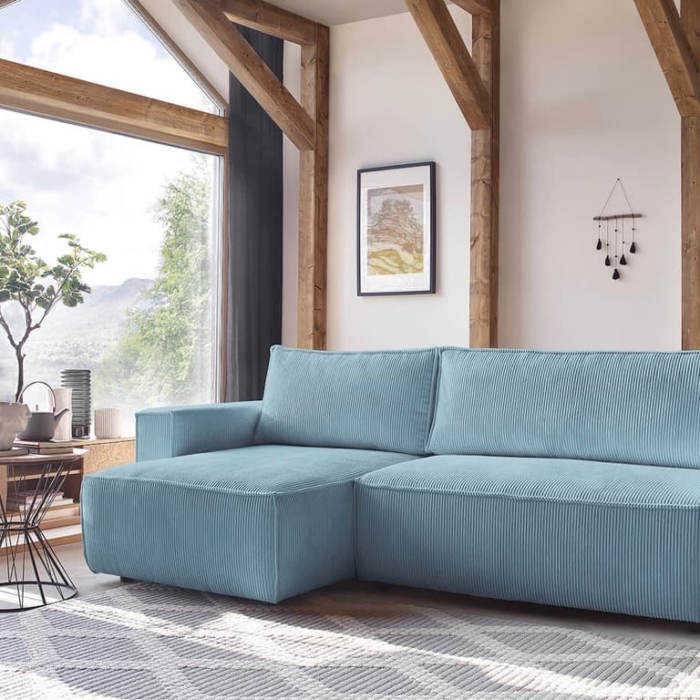 Canapé d’angle bleu en velours côtelé avec coussins dans un salon lumineux