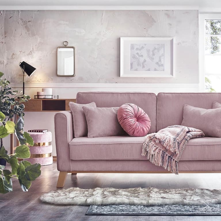 Coussins roses sur un canapé gris avec tapis et plaid en fausse fourrure