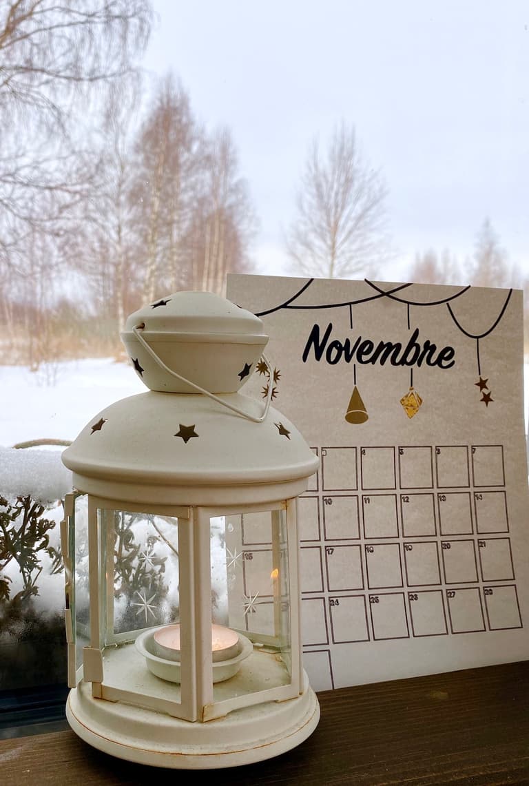 Calendrier de novembre décoré d’un feuillage noir près d’une lanterne et d’une fenêtre enneigée
