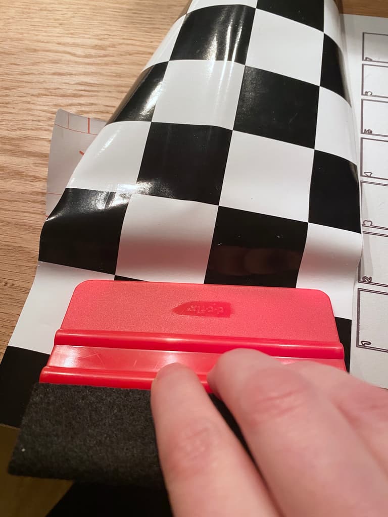 Lissage d’un adhésif noir et blanc avec une spatule rouge pour éviter les bulles