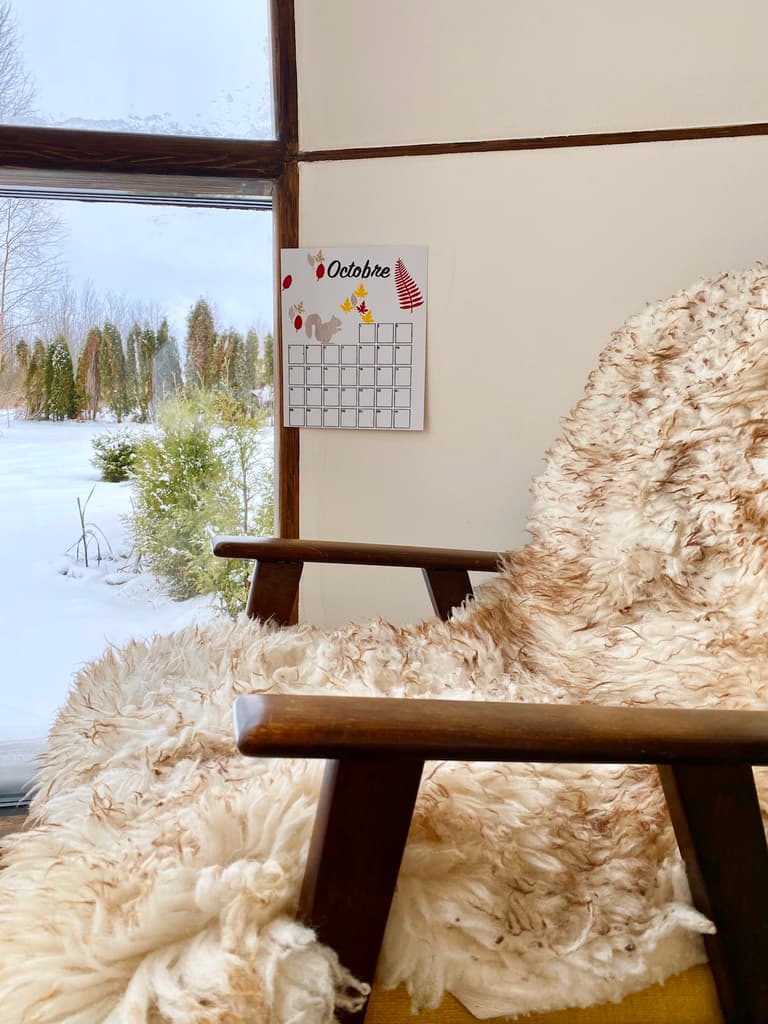 Calendrier mural de novembre installé près d’un fauteuil couvert de plaids face à une fenêtre