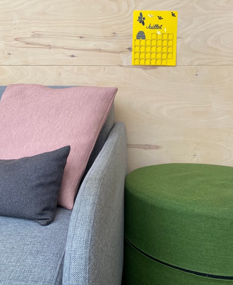 Calendrier jaune fixé sur un mur en bois clair au-dessus d’un canapé aux coussins pastel