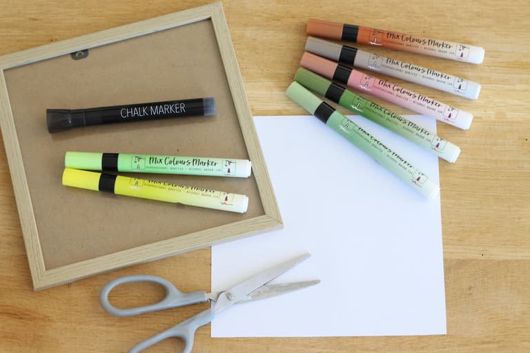 Cadre carré ouvert entouré de papier blanc, ciseaux et marqueurs colorés