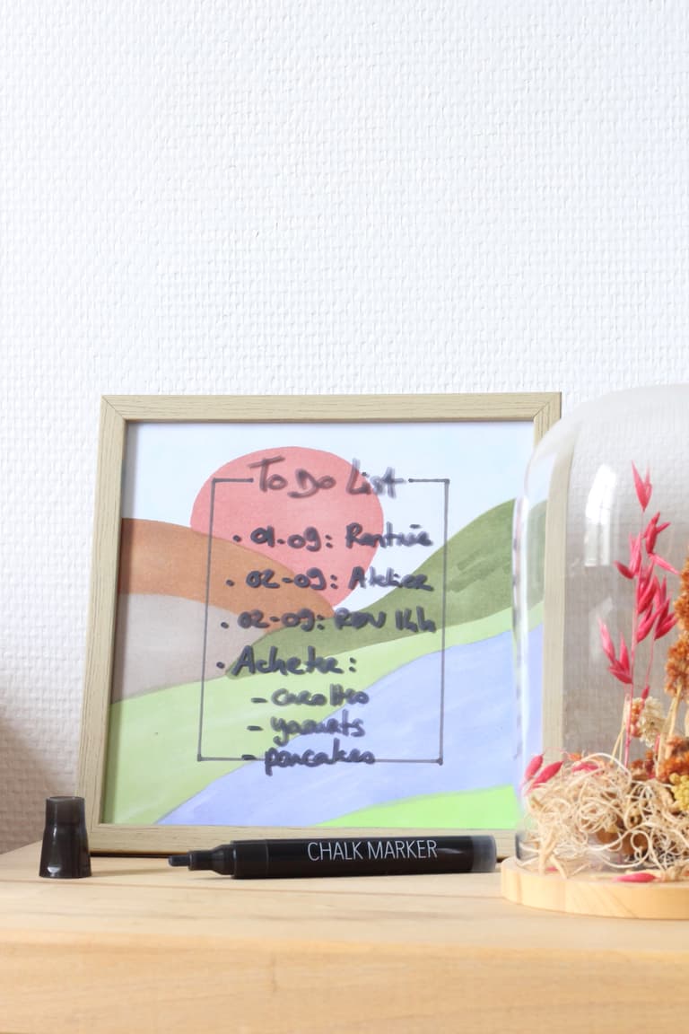 Tableau to do list coloré posé sur une étagère à côté d’une cloche en verre