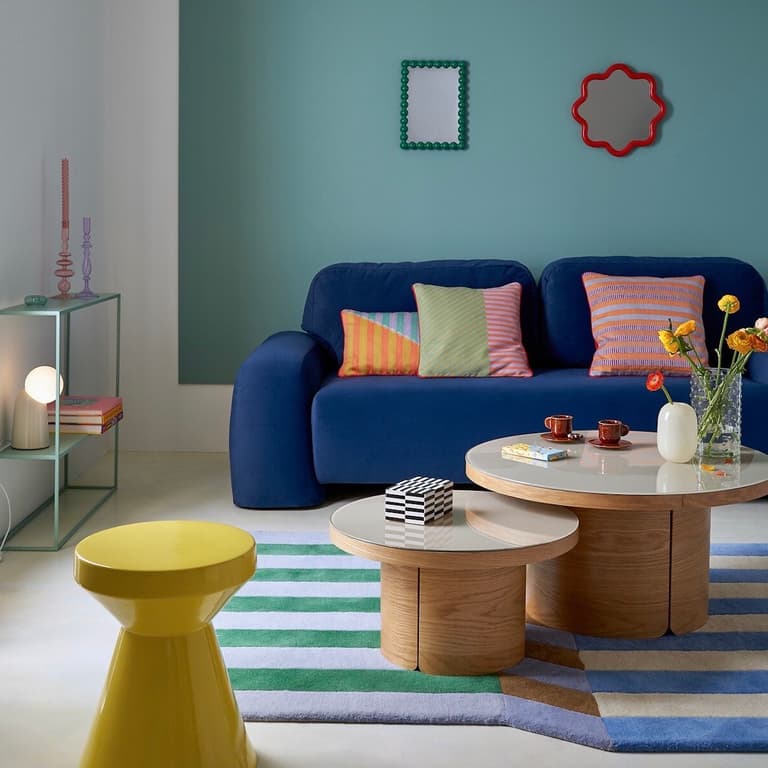 Salon coloré inspiré des années 80 avec canapé bleu, miroirs verts et coussins graphiques