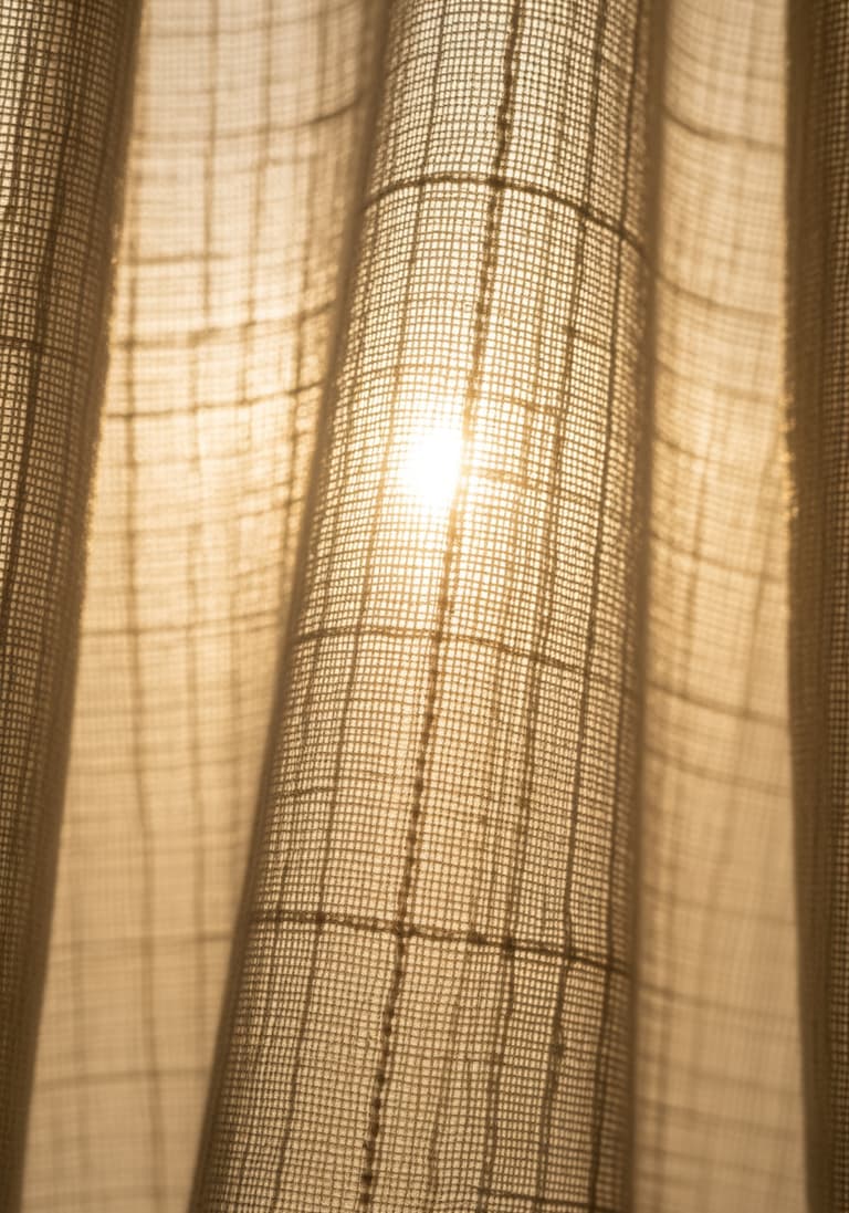 Gros plan sur la texture d'un tissu de voilage en gaze de coton, avec la lumière du soleil qui le traverse et en révèle le tissage.