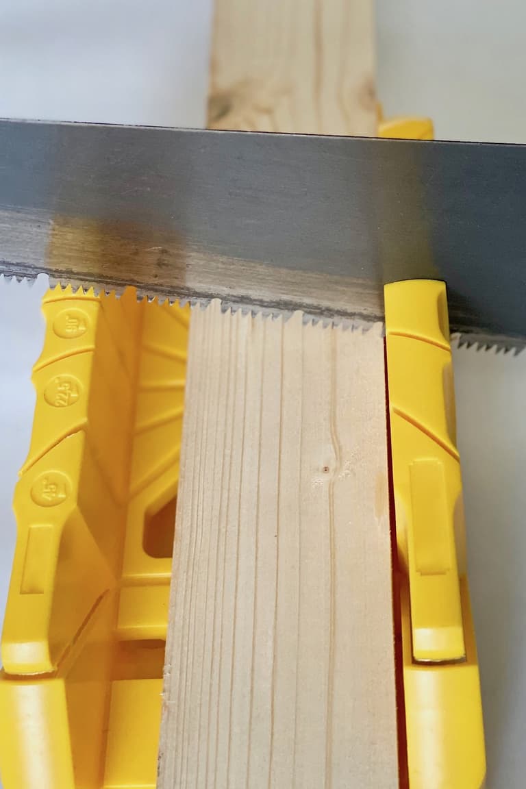 Tasseau de pin maintenu dans une boîte à onglets jaune pendant sa découpe avec une scie manuelle