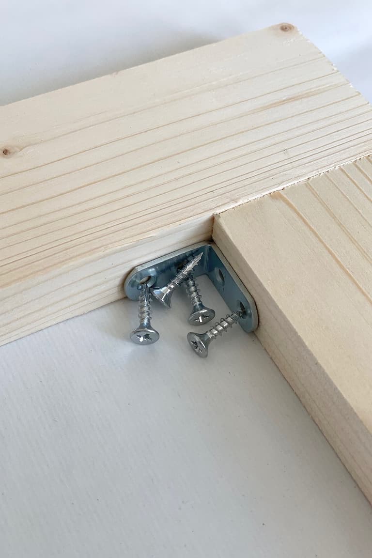 Équerre métallique placée dans l’angle de deux tasseaux de pin avec les vis prêtes pour l’assemblage