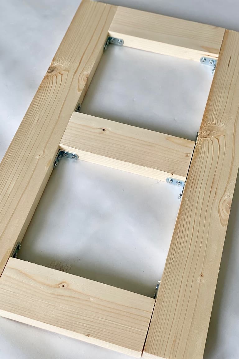 Structure rectangulaire du porte-gamelle assemblée en pin avec trois traverses et des équerres métalliques