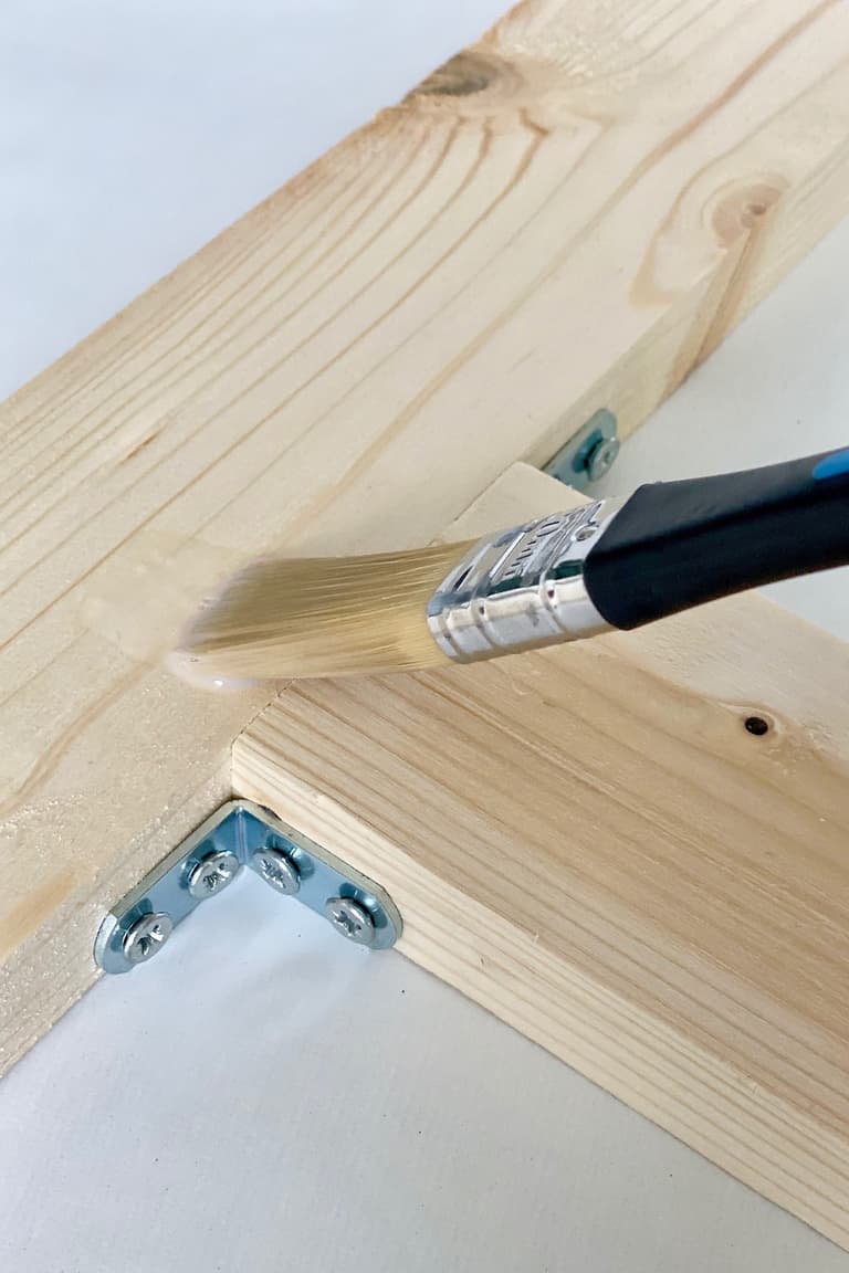 Pinceau appliquant du vernis incolore sur la structure en pin assemblée du porte-gamelle