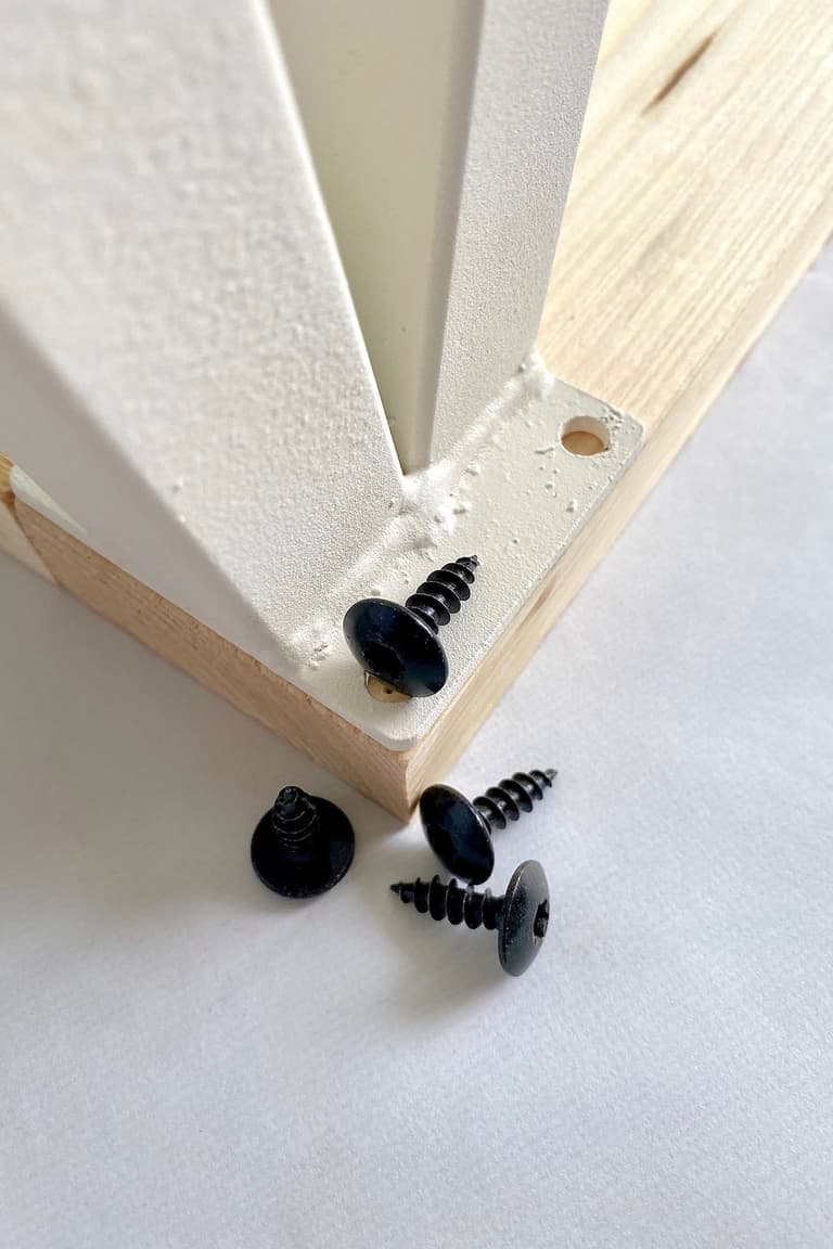 Pied de meuble blanc positionné sous le porte-gamelle en bois avec ses vis noires