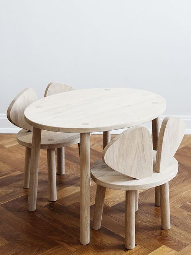 Table ovale basse en bois clair avec quatre petites chaises adaptées à la taille des enfants.