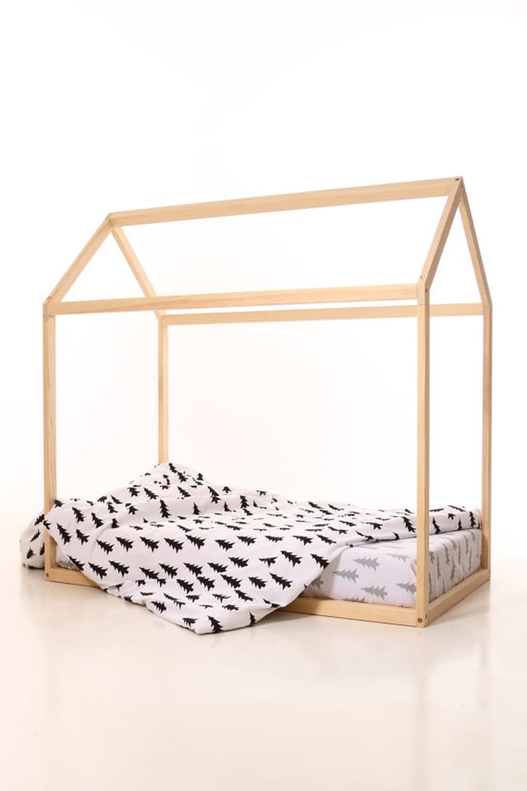 Lit cabane bas en bois naturel avec matelas au sol et couette à motifs dans une chambre d’enfant.