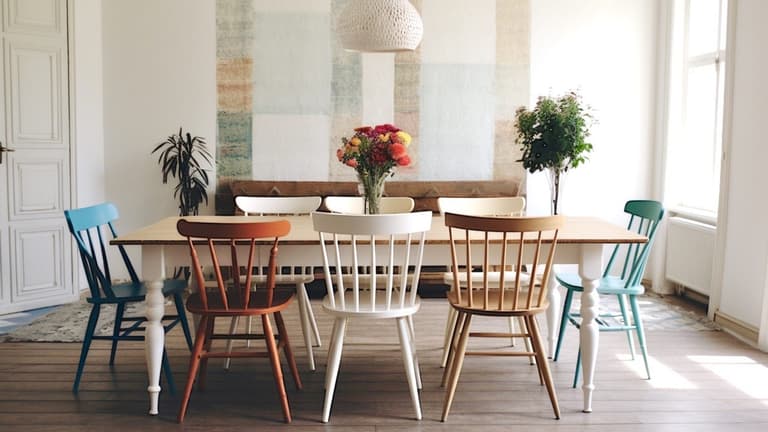 salle à manger lumineuse avec table en bois et chaises dépareillées blanches, bleues, vertes et terracotta