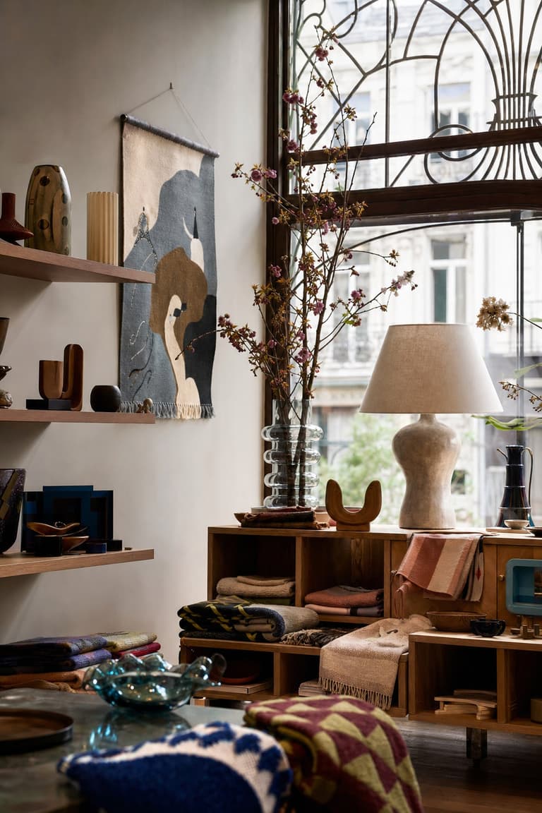 concept store déco à Bruxelles avec textiles colorés, lampe sculpturale, livres d’art et fenêtre Art Nouveau