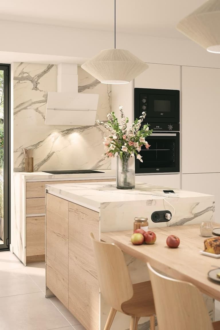 Première cuisine équipée lumineuse avec façades en bois clair, plan de travail effet marbre, îlot central et électroménager noir encastré