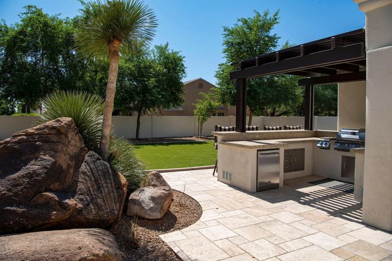 Cuisine extérieure maçonnée avec barbecue en inox sous une pergola, au bord d’un jardin paysager.