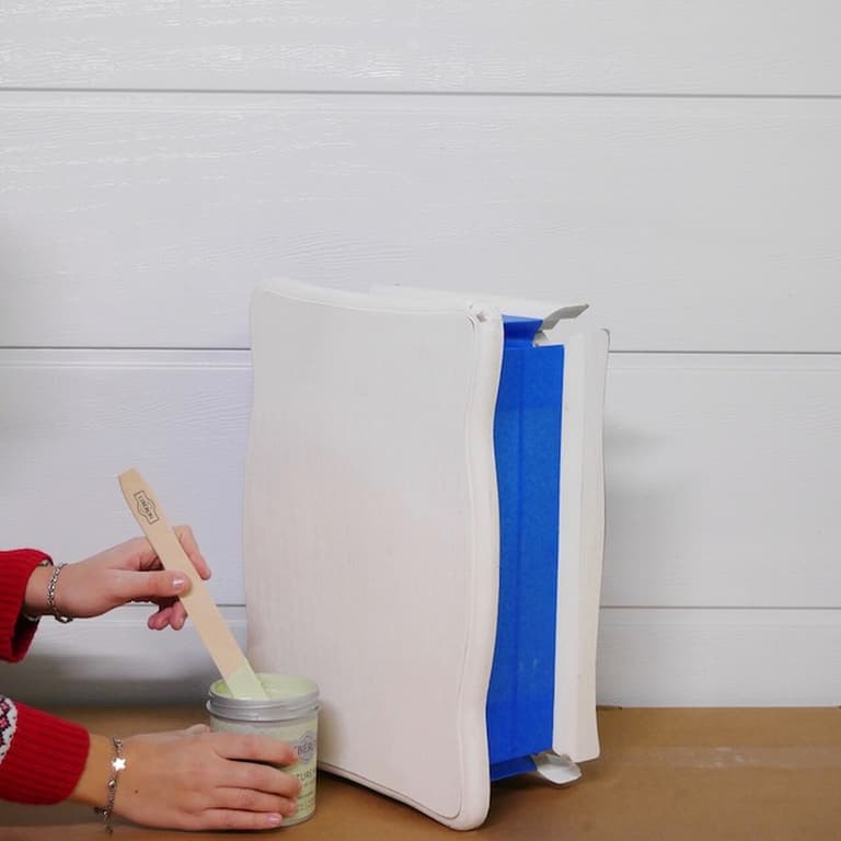 Mélange d’une peinture vert clair devant une table de chevet protégée par du ruban bleu
