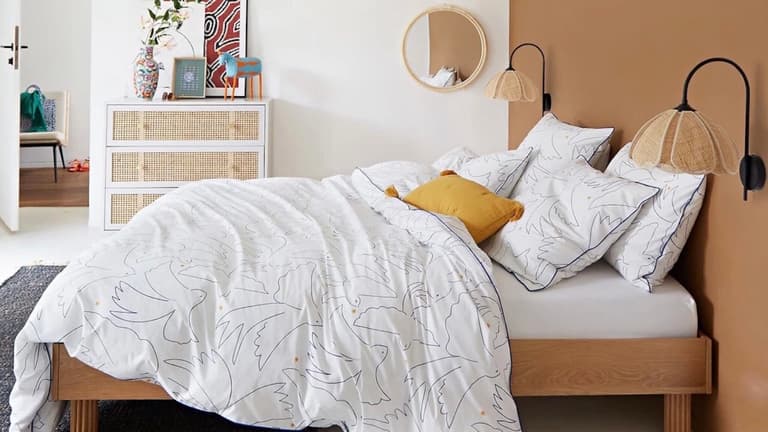 Chambre chaleureuse avec lit en bois, parure de lit blanche à motifs, lampes en rotin et coussin jaune