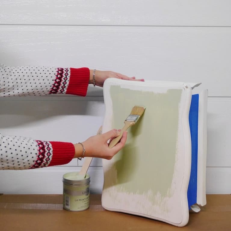 Application au pinceau d’une peinture vert clair sur le côté de la table de chevet