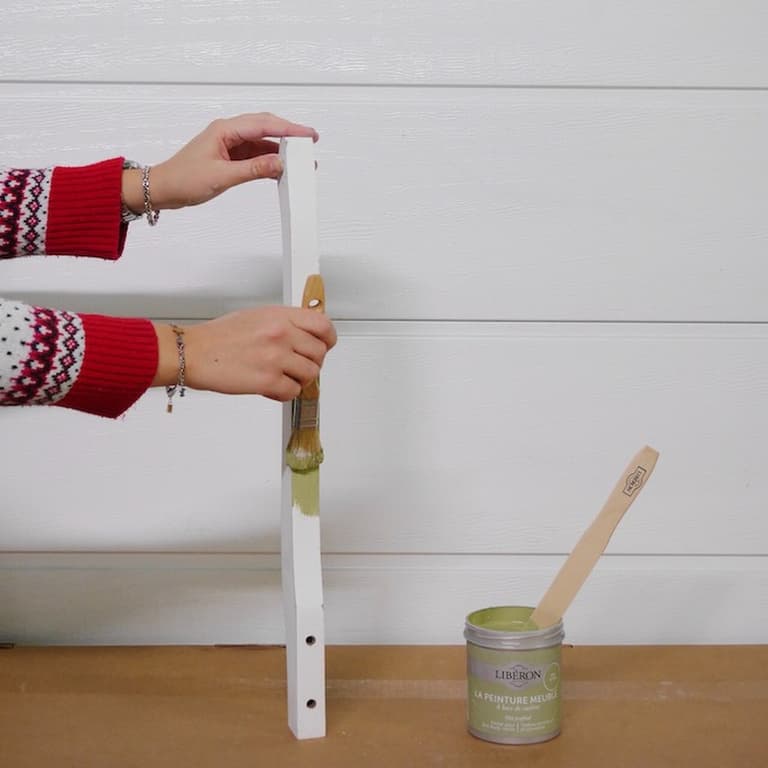 Application de peinture verte sur une fine traverse démontée de la table de chevet