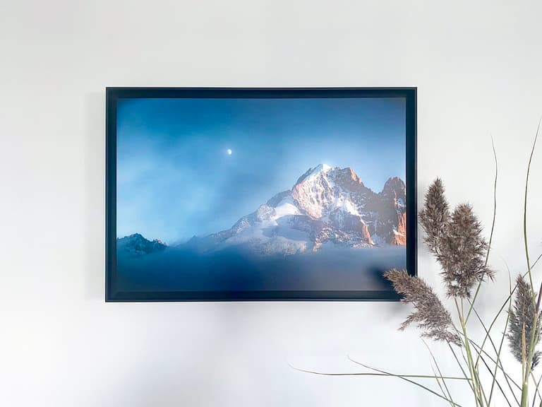 Photographie encadrée de l’Aiguille Verte éclairée par le soleil couchant, avec la lune dans un ciel bleu-gris