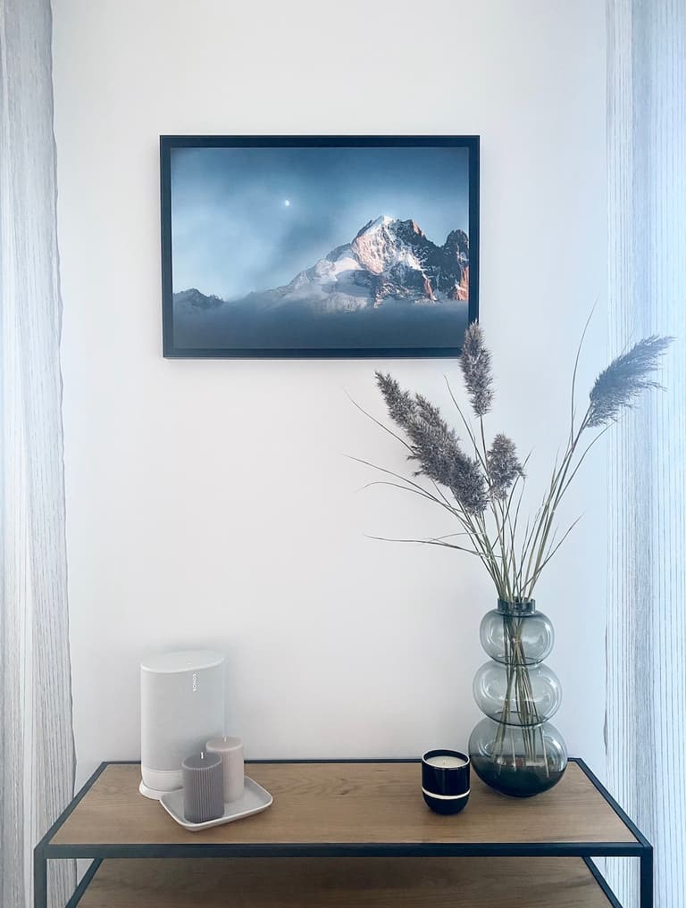 Photographie encadrée de l’Aiguille Verte au-dessus d’une console en bois décorée de bougies et d’un vase de fleurs séchées