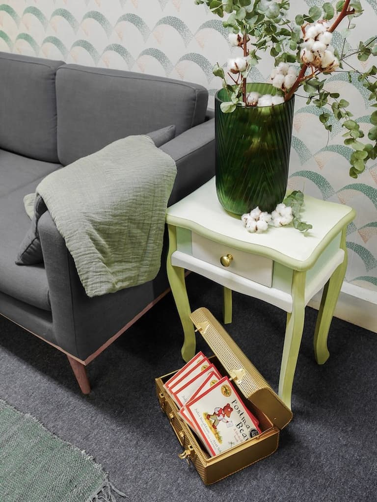 Table de chevet relookée en vert et blanc avec un vase de fleurs près d’un canapé gris