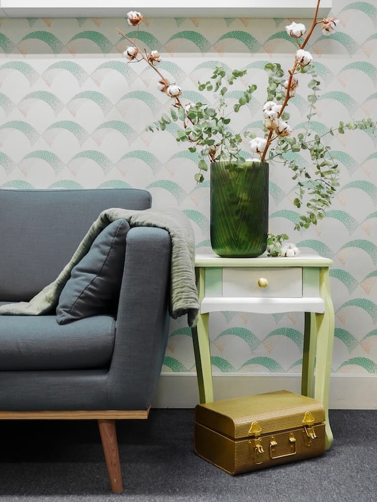 Table de chevet verte et blanche avec poignée dorée, vase fleuri et petite valise