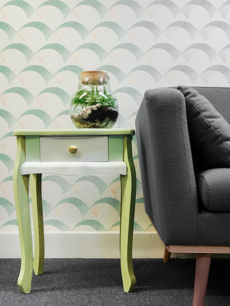 Table de chevet verte et blanche avec poignée dorée et terrarium entre deux fauteuils gris