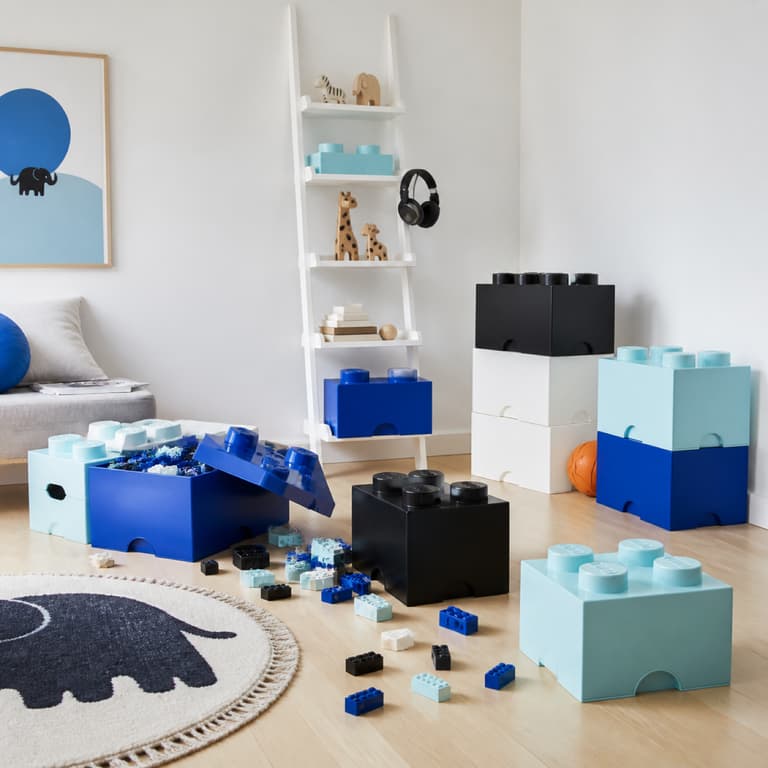 Chambre d’enfant blanche avec rangements bleus et aqua en forme de briques et jouets au sol.