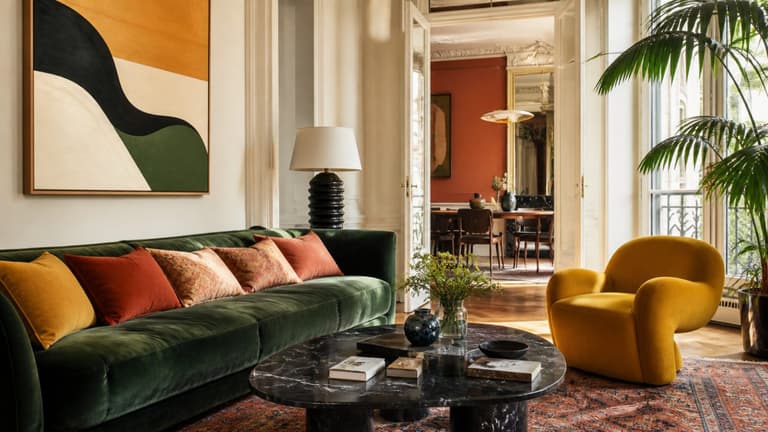 Salon lumineux avec canapé vert émeraude, fauteuil jaune, tapis graphique et touches terracotta dans un intérieur parisien
