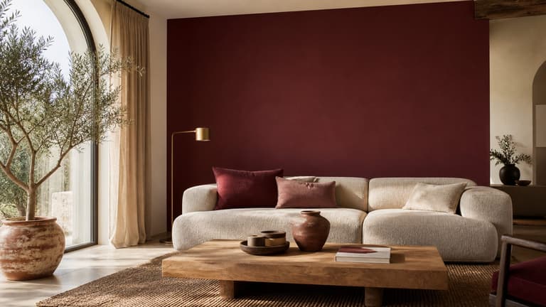 Salon contemporain avec mur marsala, canapé beige, table basse en bois clair et accessoires terracotta
