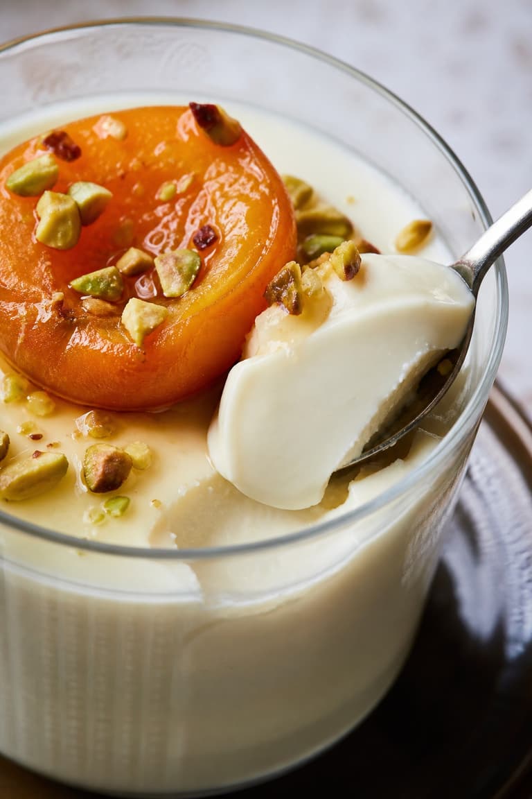 Cuillère prélevant une panna cotta ivoire crémeuse avec un abricot rôti, des pistaches et du miel