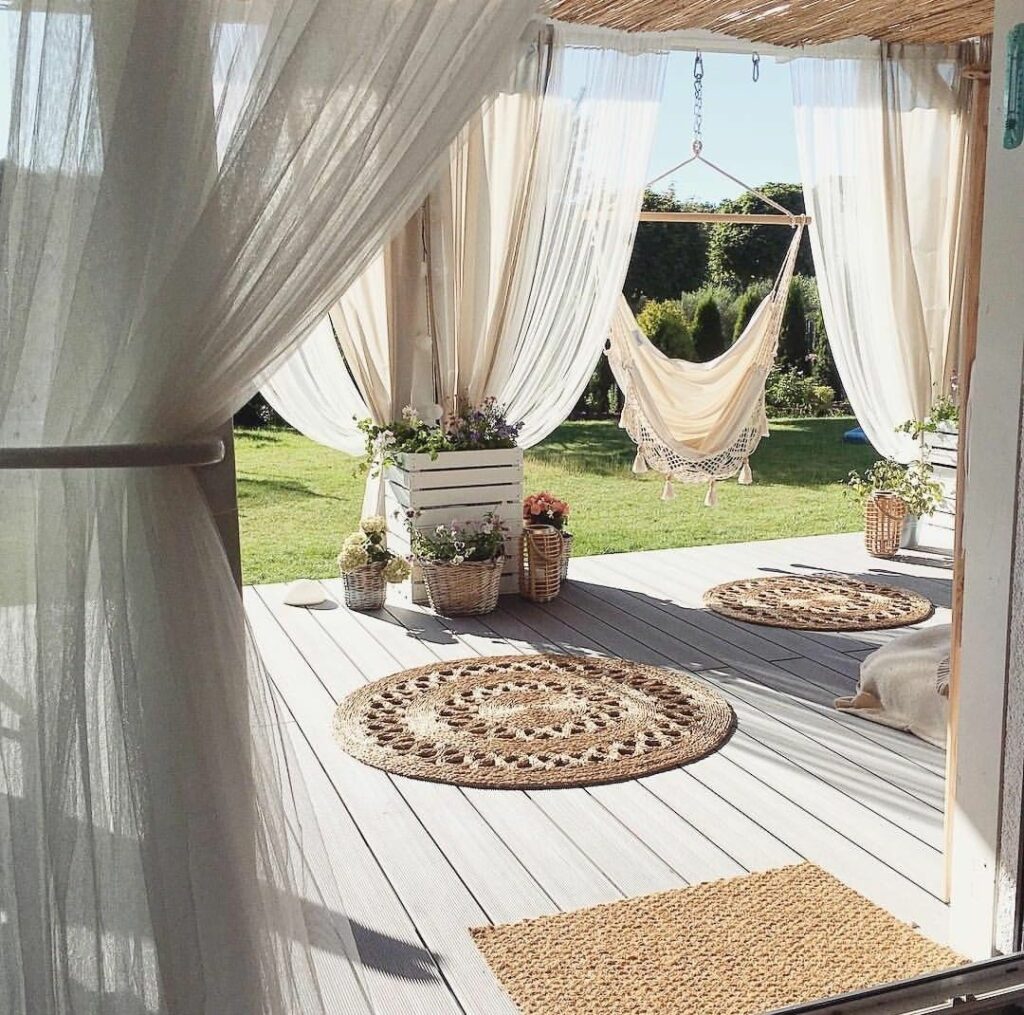 extérieur bohème chic voile rideau blanc tapis rond osier terrasse en bois hamac à pompon