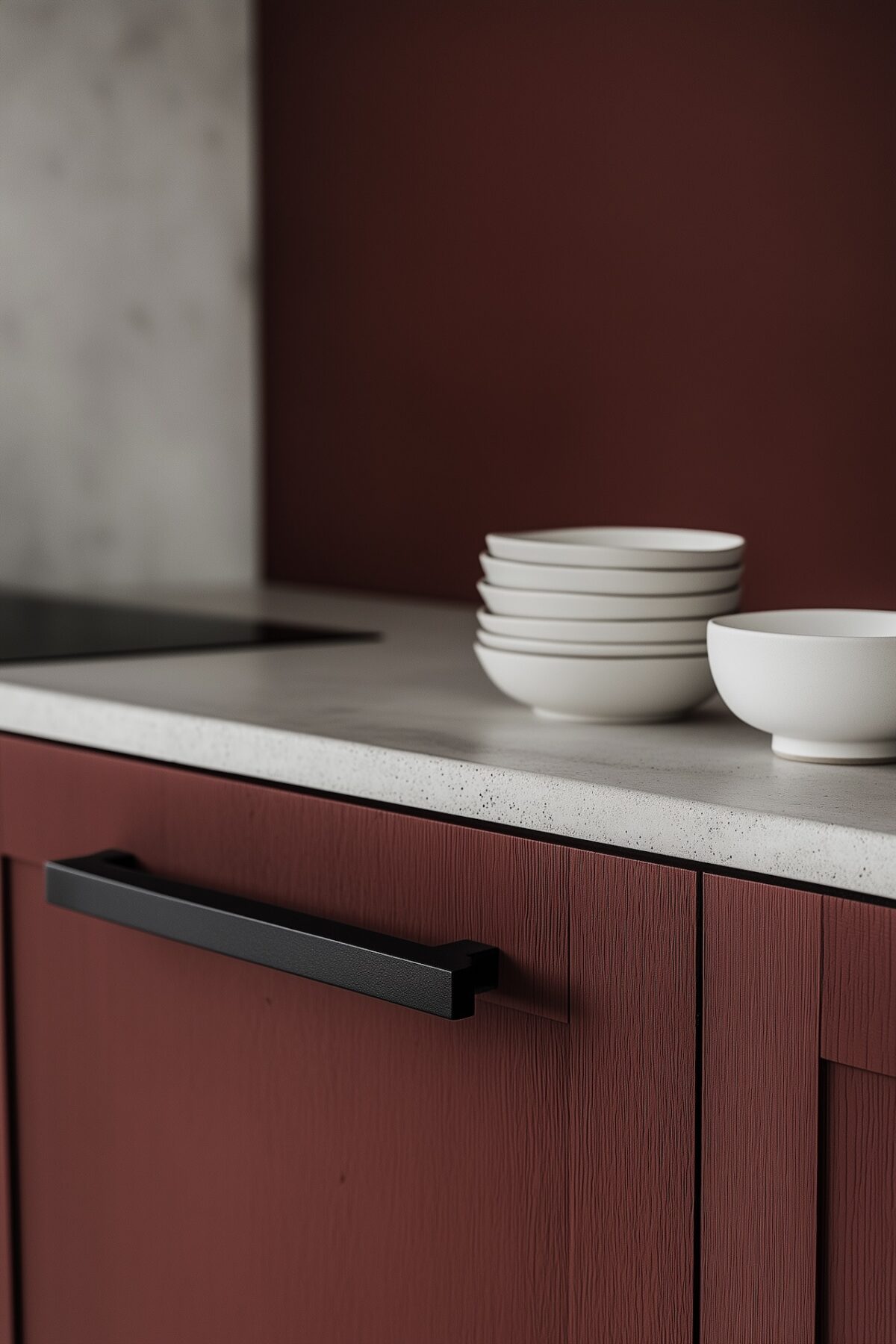 façade de cuisine rouge mat texturée avec poignée noire rectangulaire, plan de travail en pierre claire mouchetée, pile d'assiettes et bol en céramique blanche, mur rouge en arrière-plan flou