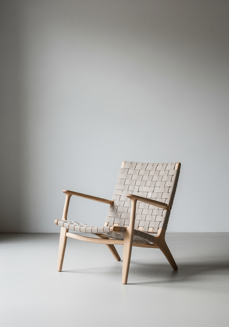 Un fauteuil design en bois clair, pièce maîtresse d'une marque de mobilier française, présenté dans un décor minimaliste.