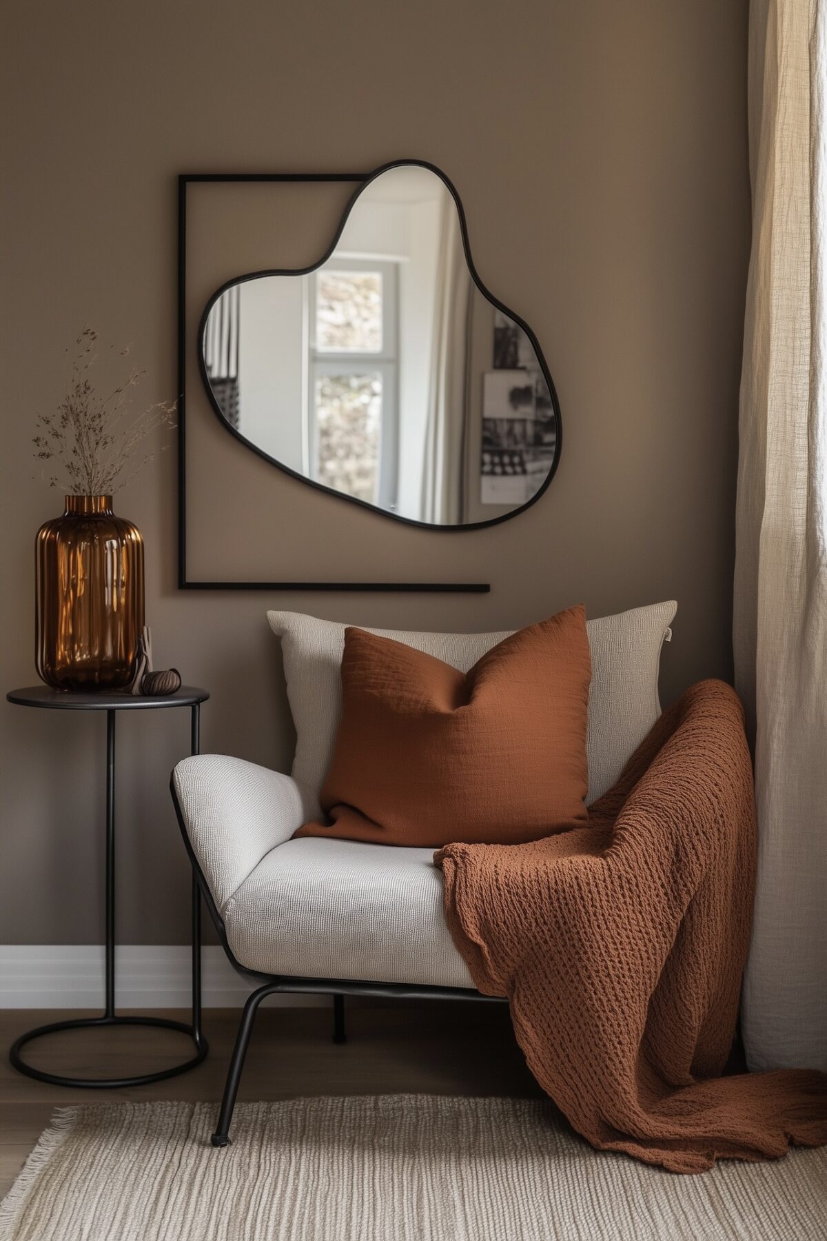 Coin lecture stylé à petit budget avec fauteuil crème et plaid terracotta, coussin assorti, miroir organique au mur, table d'appoint en métal noir avec vase en verre ambré, rideau en lin, tapis clair