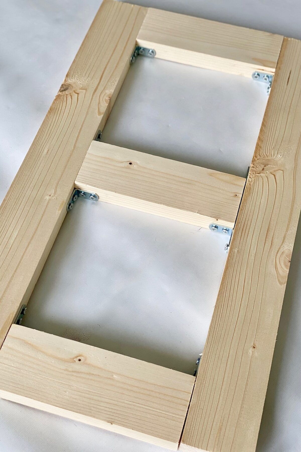 Structure rectangulaire du porte-gamelle assemblée en pin avec trois traverses et des équerres métalliques