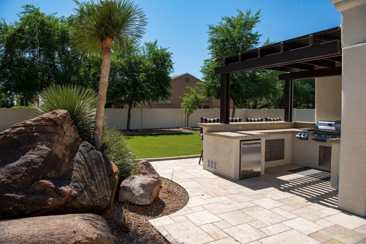 Cuisine extérieure maçonnée avec barbecue en inox sous une pergola, au bord d’un jardin paysager.